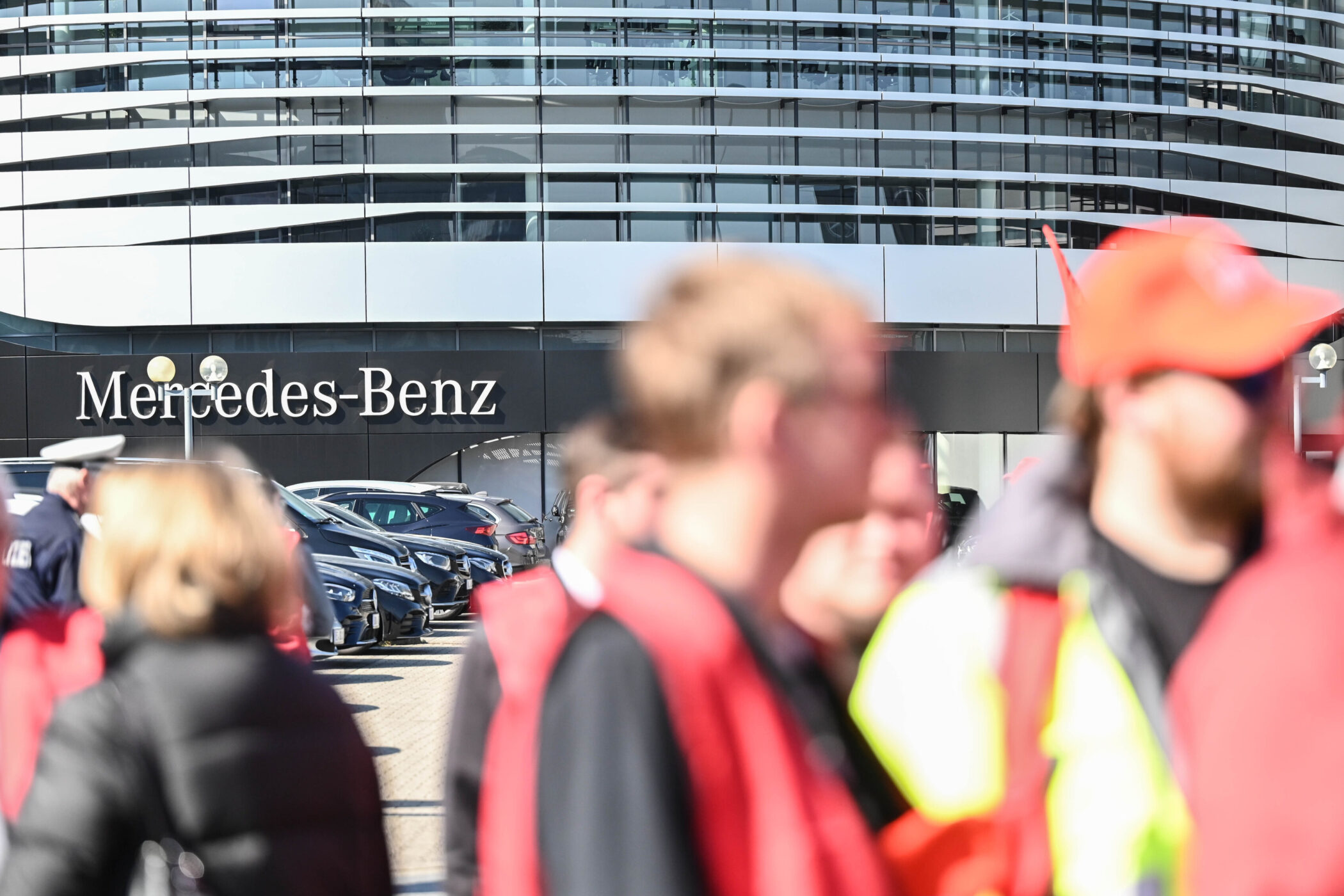Mehrere Personen vor einem Mercedes-Benz-Gebäude. Autos im Hintergrund.
