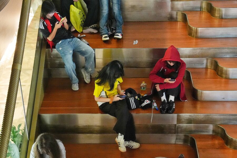 Vier Personen sitzen auf Holzbänken, alle schauen auf ihre Smartphones.