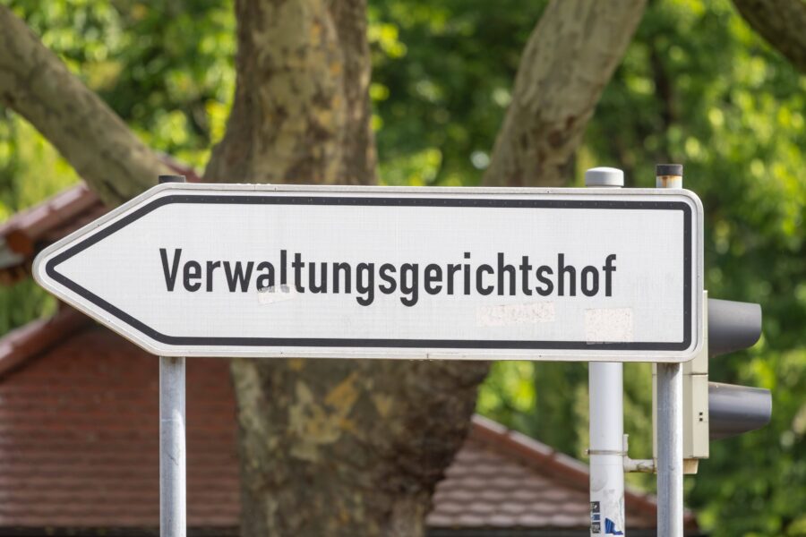 Verkehrsschild mit der Aufschrift "Verwaltungsgerichtshof", Bäume im Hintergrund.