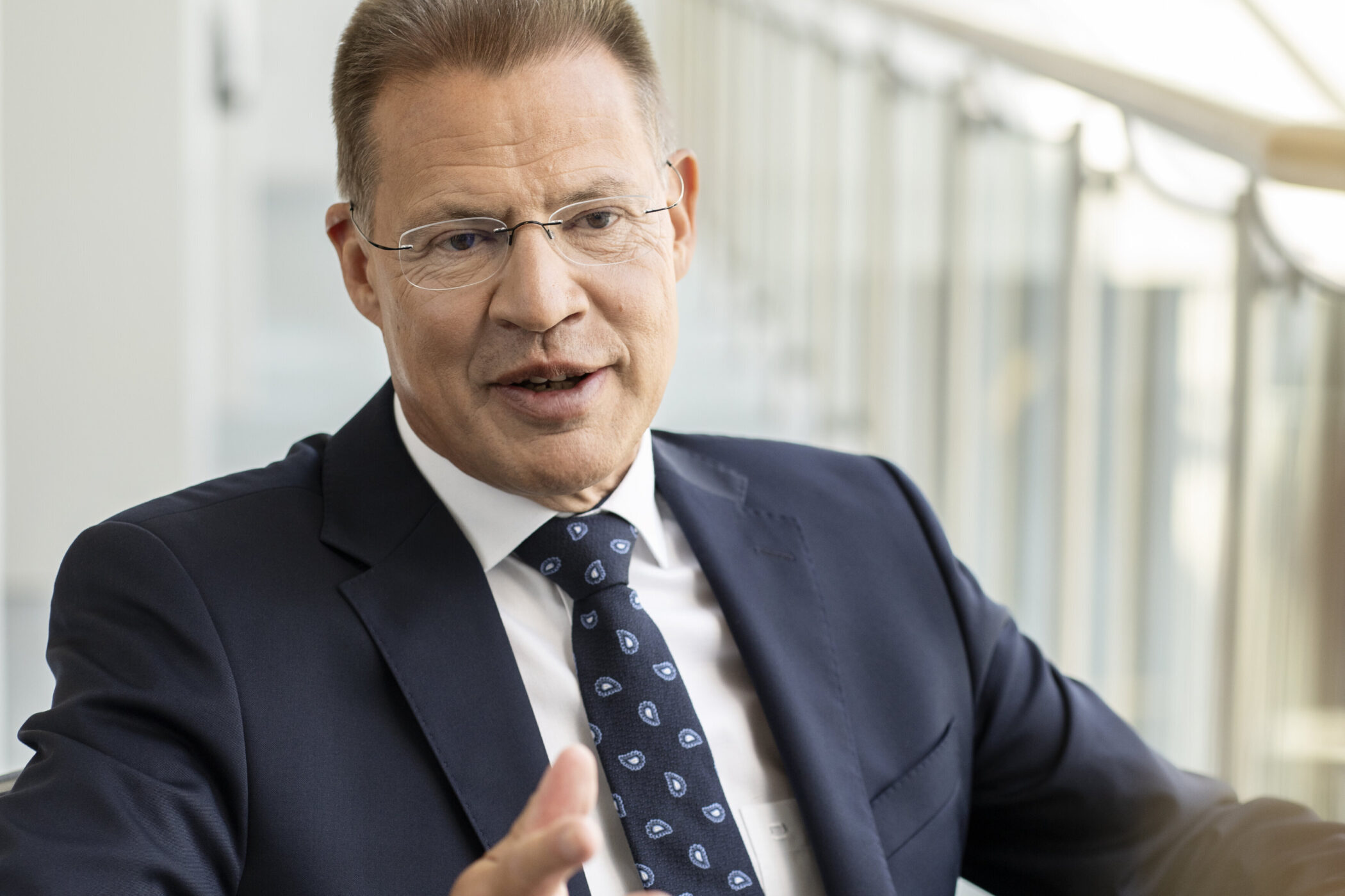 Ein Mann im Anzug spricht, im Hintergrund Glasgeländer.