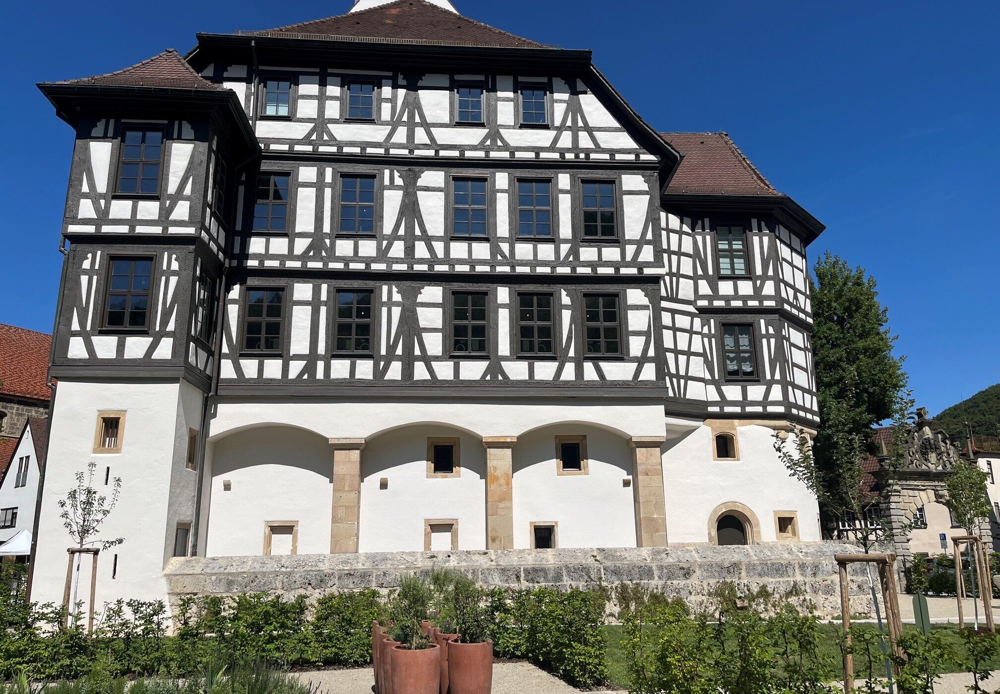 Fachwerkgebäude mit weißer Fassade, dahinter blauer Himmel, vorne Gartenanlage.
