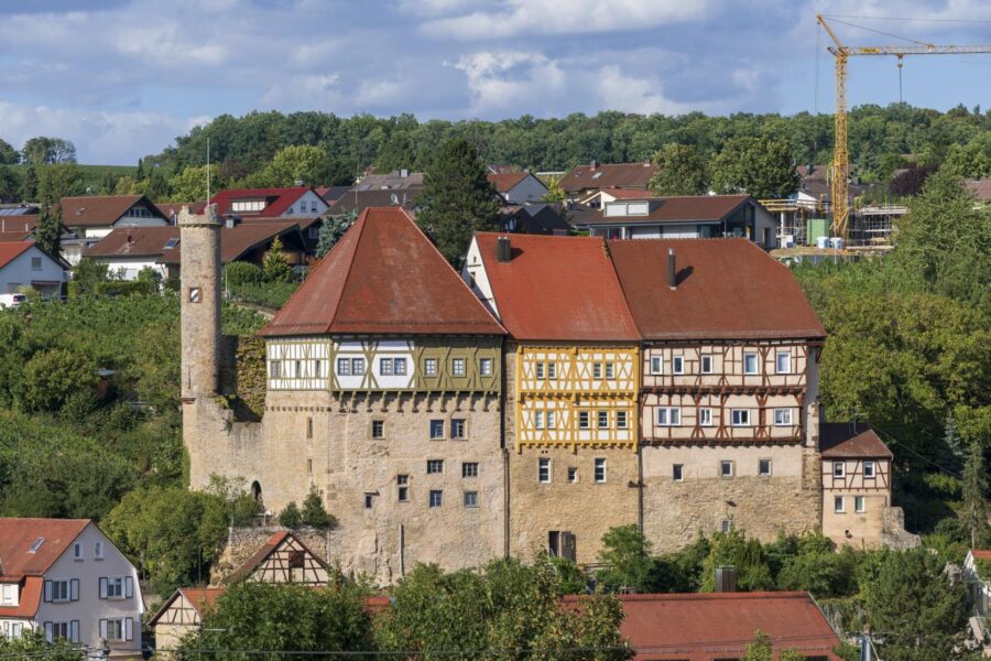 Fachwerkgebäude mit rotem Dach und Turm, im Hintergrund Wohnhäuser und Baukran.