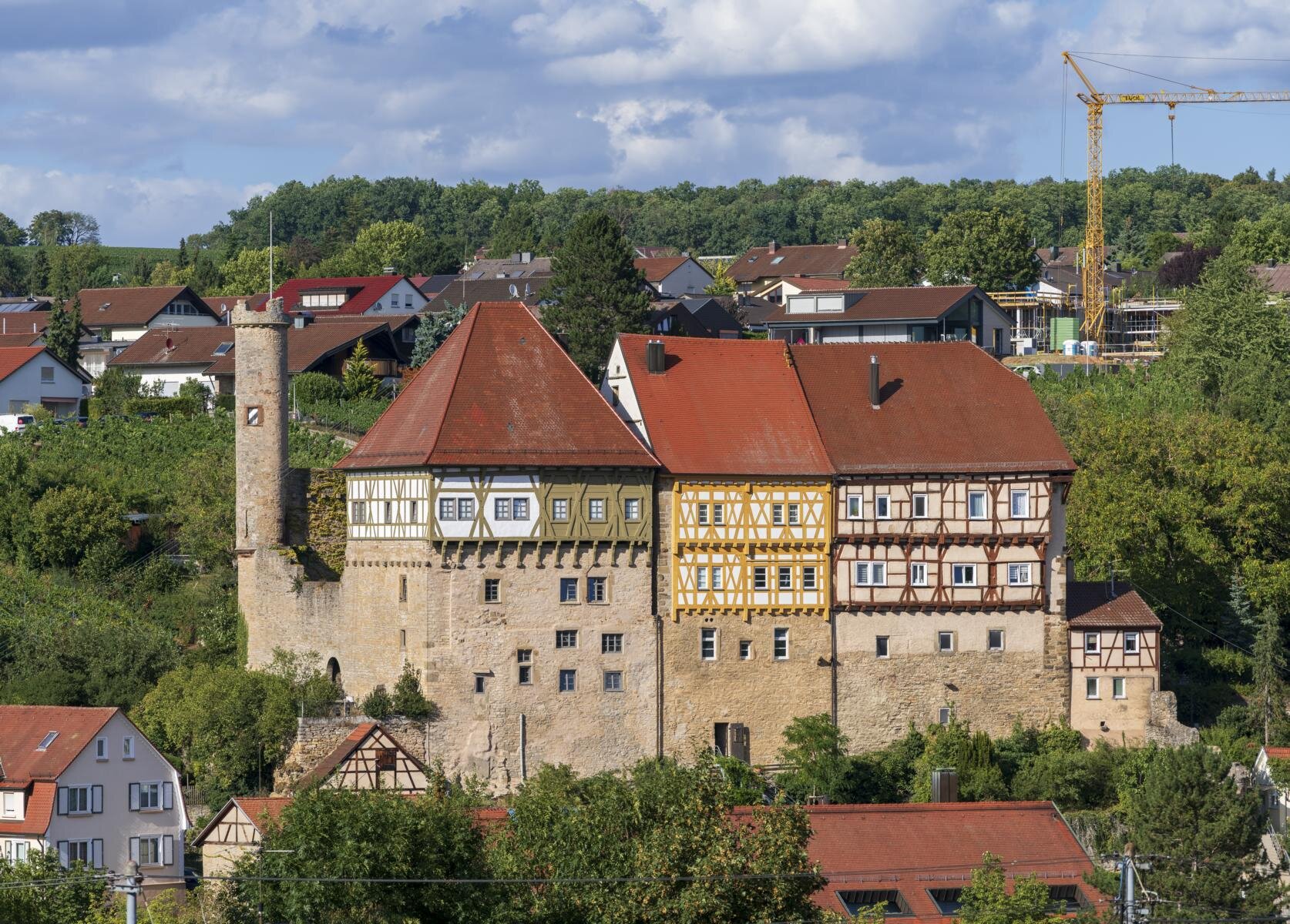 Fachwerkgebäude mit rotem Dach und Turm, im Hintergrund Wohnhäuser und Baukran.