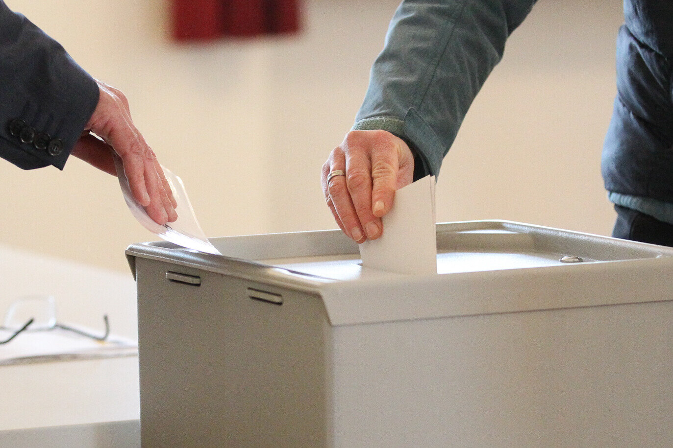 Zwei Hände werfen Wahlzettel in eine Metall-Urne.
