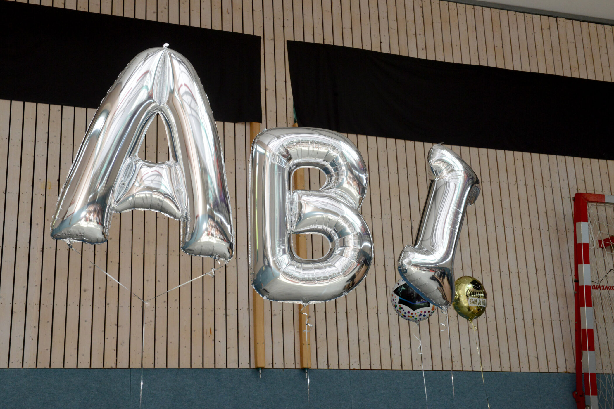 Silberne Luftballons formen das Wort "ABI" vor Holzwand.
