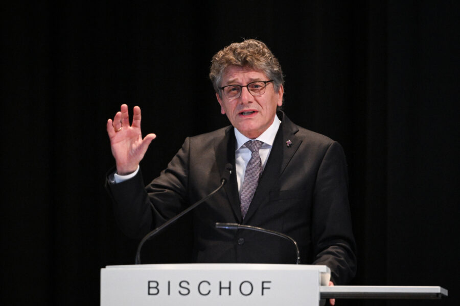 Ein Mann in Anzug spricht am Pult mit der Aufschrift "BISCHOF".