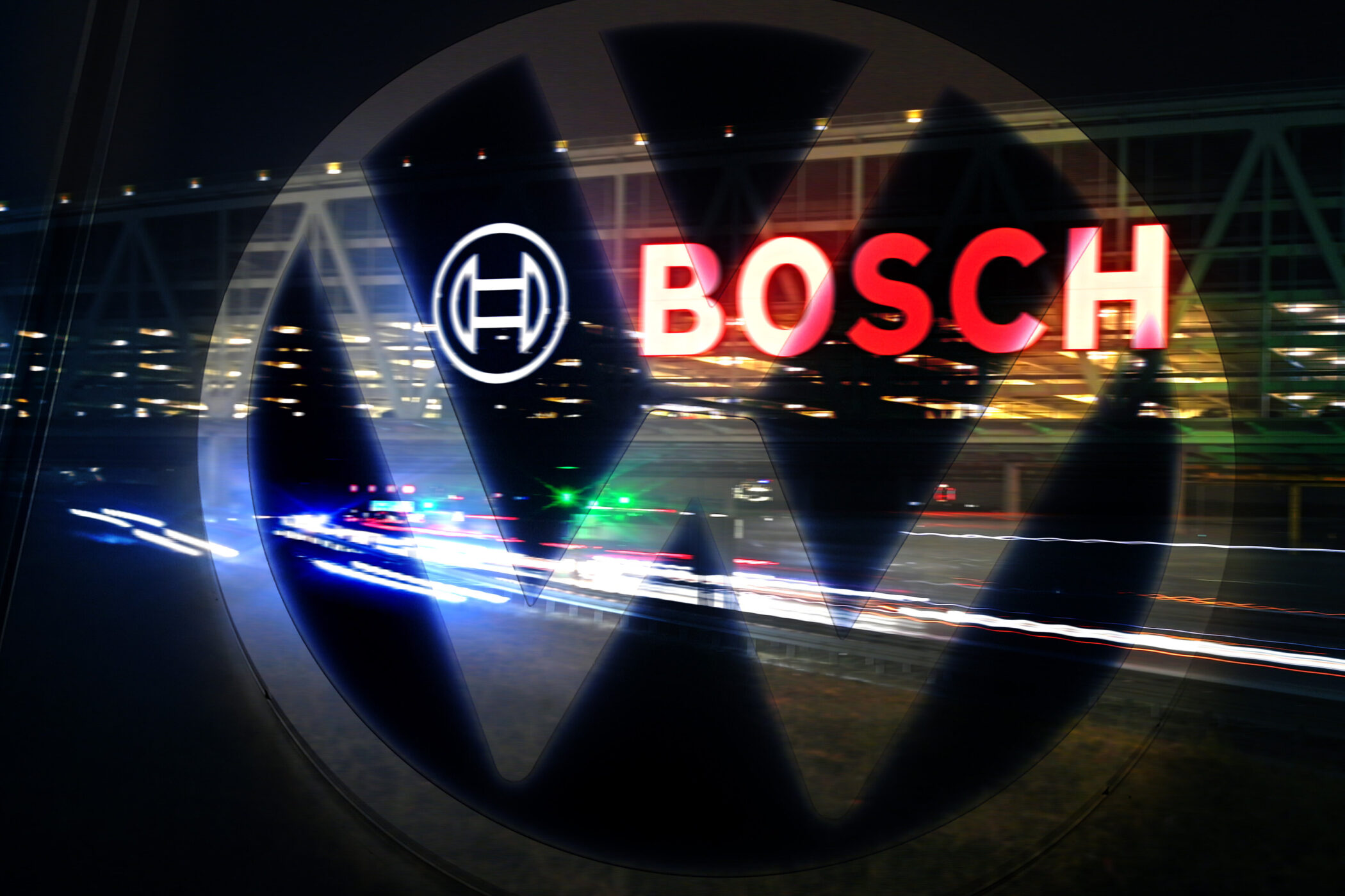 Logo von VW und Bosch, Hintergrund unscharfe Lichter, rote und weiße Lichtspuren.
