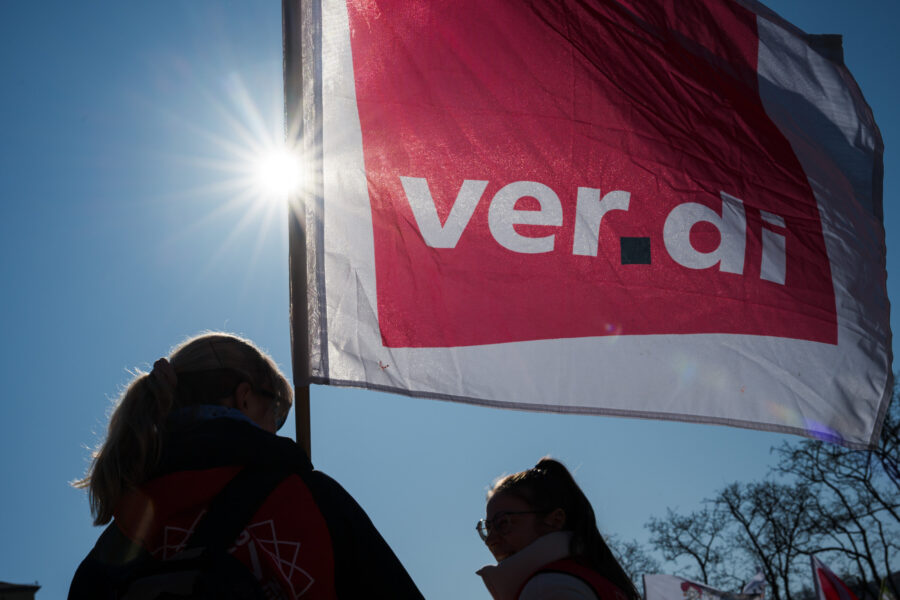 Zwei Personen neben einer wehenden Flagge mit der Aufschrift „ver.di“.