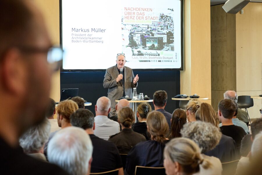 Ein Mann spricht vor einem Publikum, Präsentation auf der Leinwand.