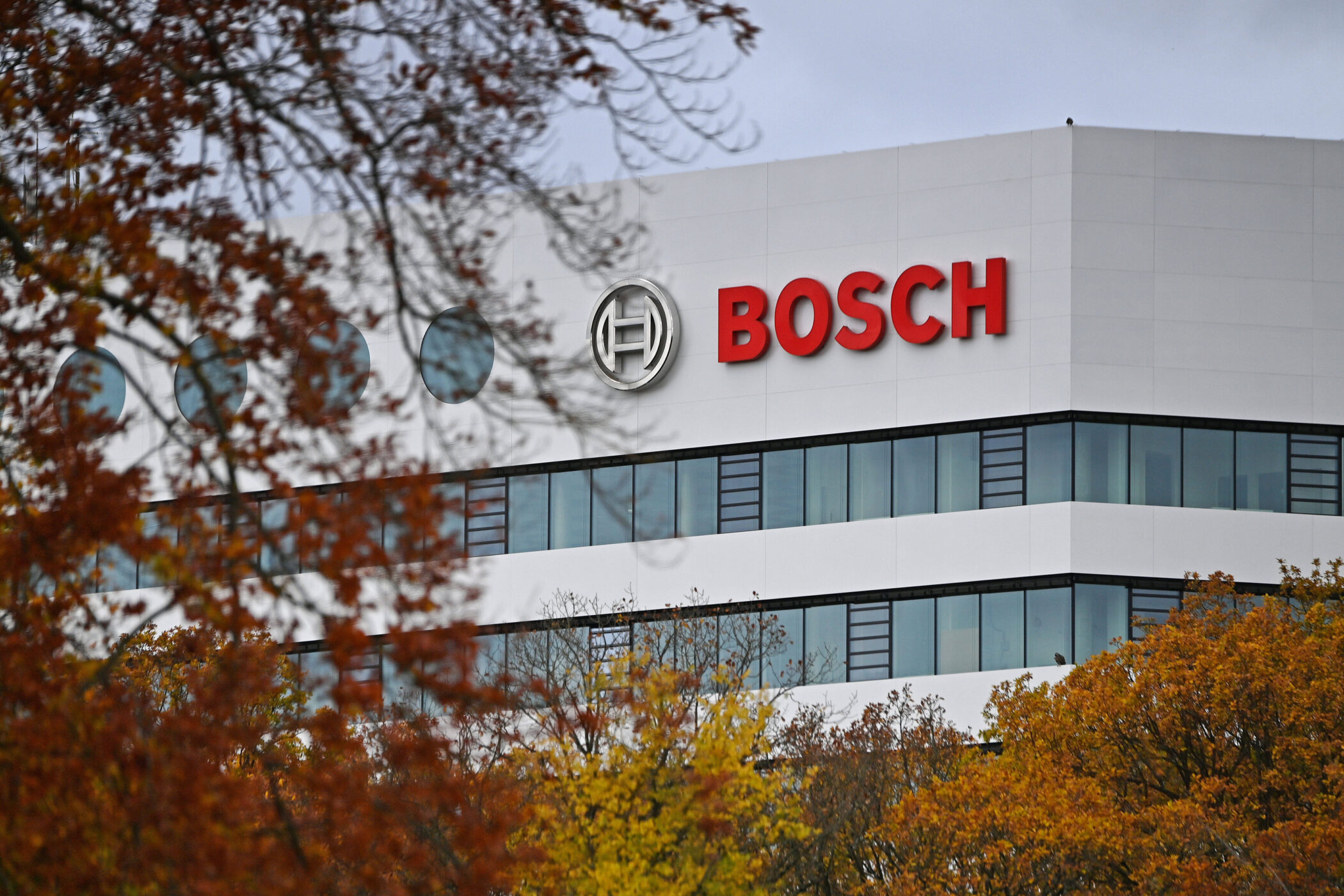 Weißes Gebäude mit Logo und rotem Schriftzug "BOSCH", Bäume im Vordergrund.