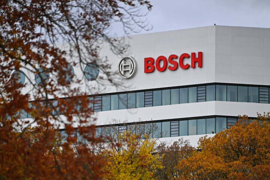 Weißes Gebäude mit Logo und rotem Schriftzug "BOSCH", Bäume im Vordergrund.