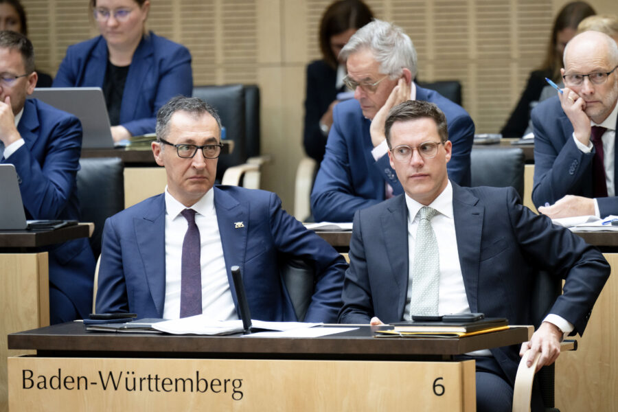 Mehrere Personen in Anzügen sitzen an Tischen. Schrift: Baden-Württemberg 6.