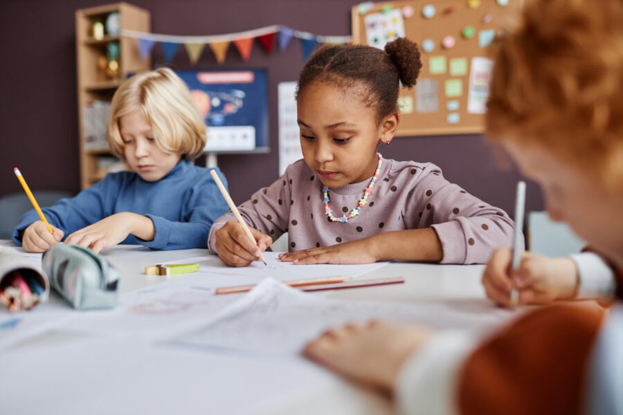 Drei Kinder sitzen an einem Tisch und schreiben auf Papier.