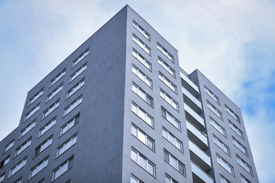 Hoher grauer Wohnblock mit vielen Fenstern und Balkonen gegen den Himmel.