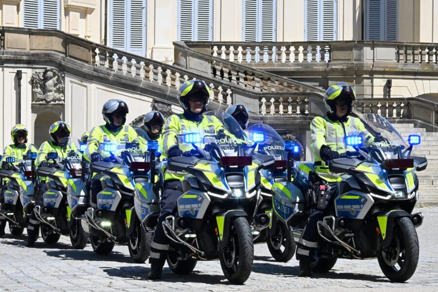 Sechs Polizisten fahren auf Motorrädern in gelben Jacken vor historischem Gebäude.
