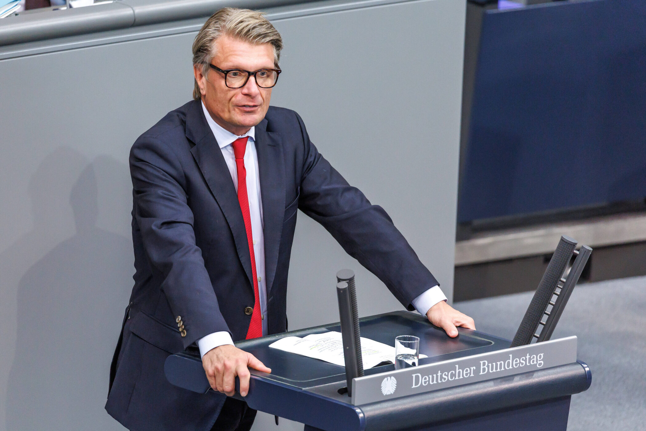 Mann im Anzug mit roter Krawatte am Rednerpult, Text: "Deutscher Bundestag".