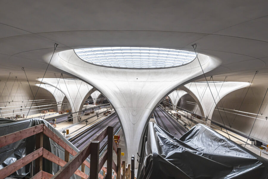 Moderne Bahnhofshalle mit großen Stützen und mehreren Gleisen.