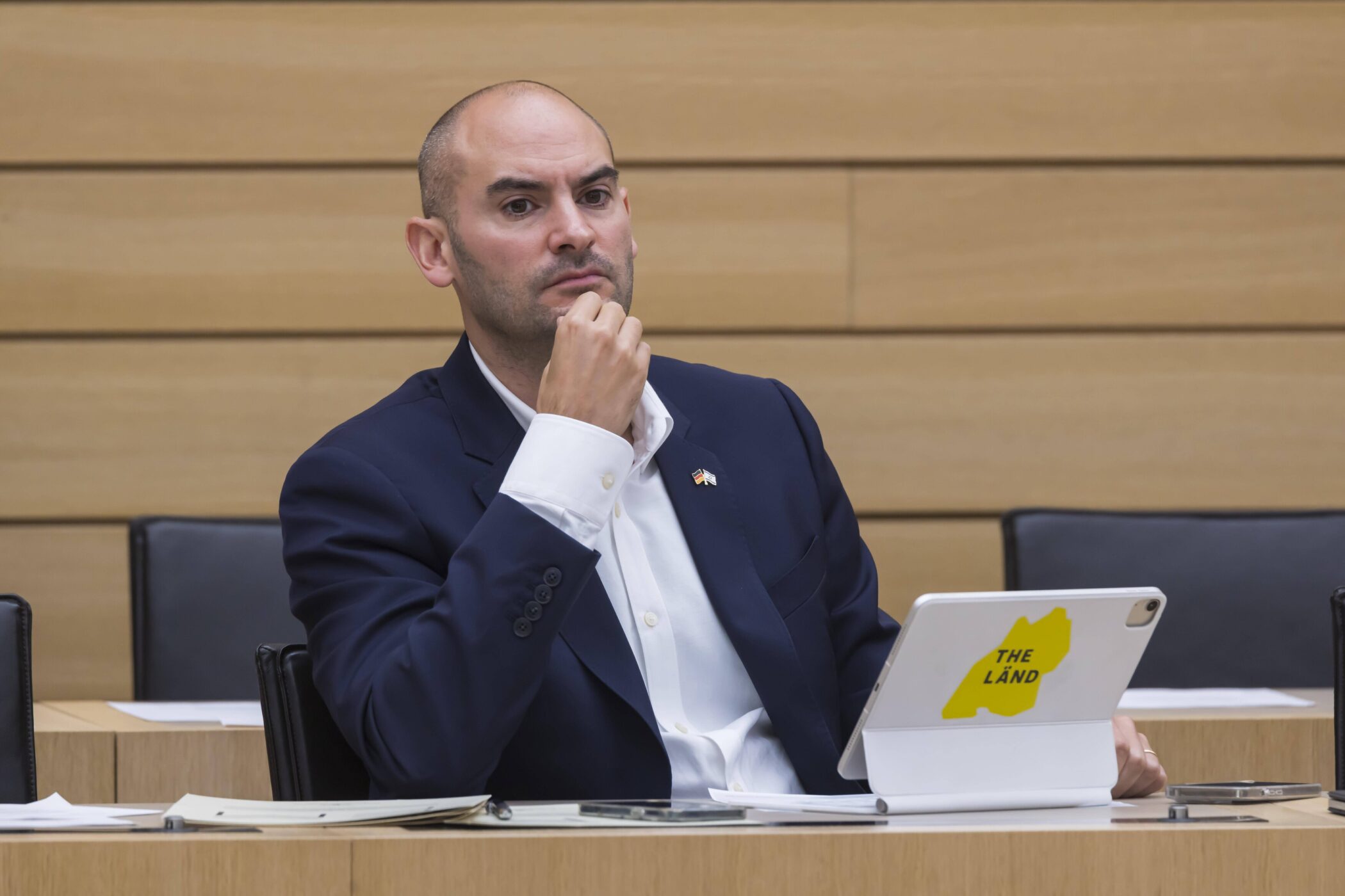 Eine Person im Anzug sitzt an einem Tisch mit Tablet, darauf "THE LÄND".