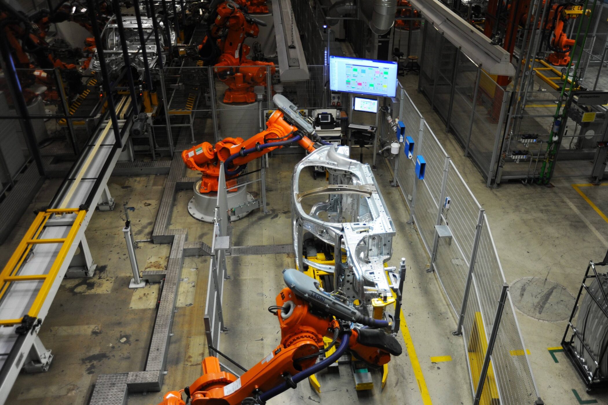 Roboterarme montieren Karosserieteile in einer Fertigungshalle.