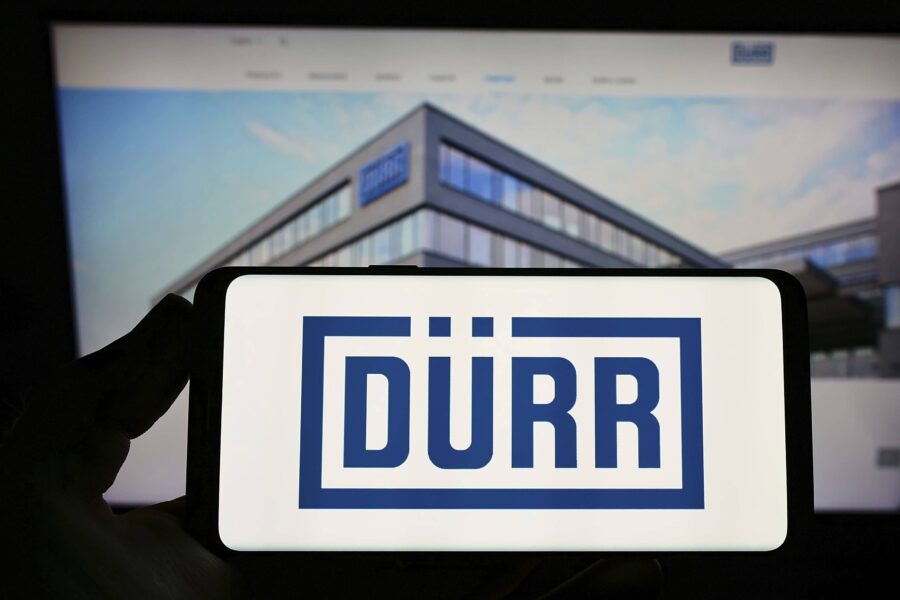 Hand hält Smartphone mit "DÜRR" Logo, Gebäude im Hintergrund.