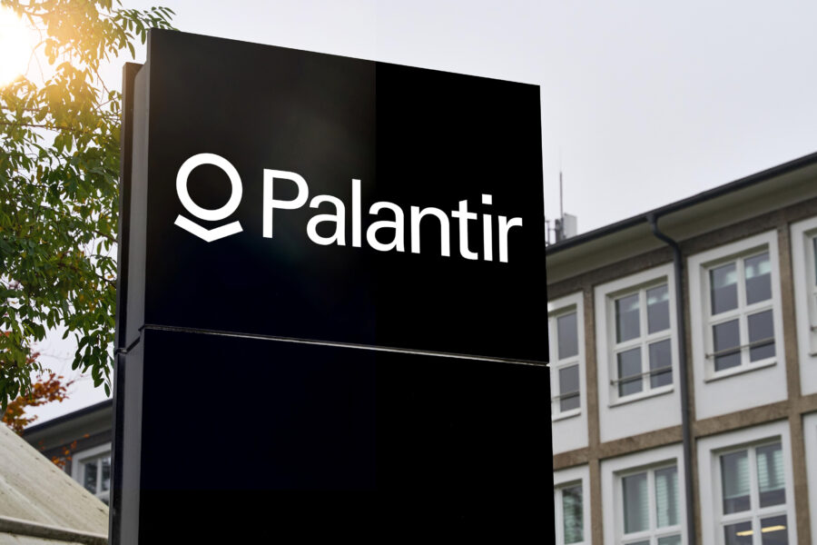 Schwarzes Schild mit weißem Text "Palantir" vor Bürogebäude.