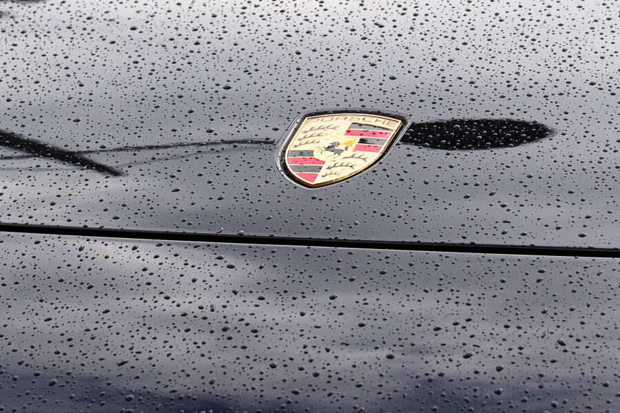 Regentropfen auf schwarzer Motorhaube mit Porsche-Emblem.