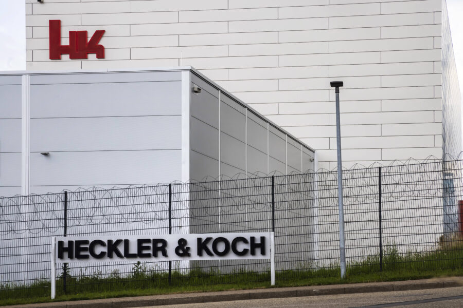 Weißes Gebäude mit rotem "HK"-Logo, Zaun mit "HECKLER & KOCH" Schriftzug.