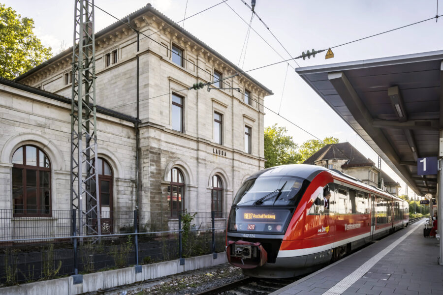 Zug am Bahnhof Lauda, Gleis 1, Ziel Aschaffenburg, graues Gebäude im Hintergrund.