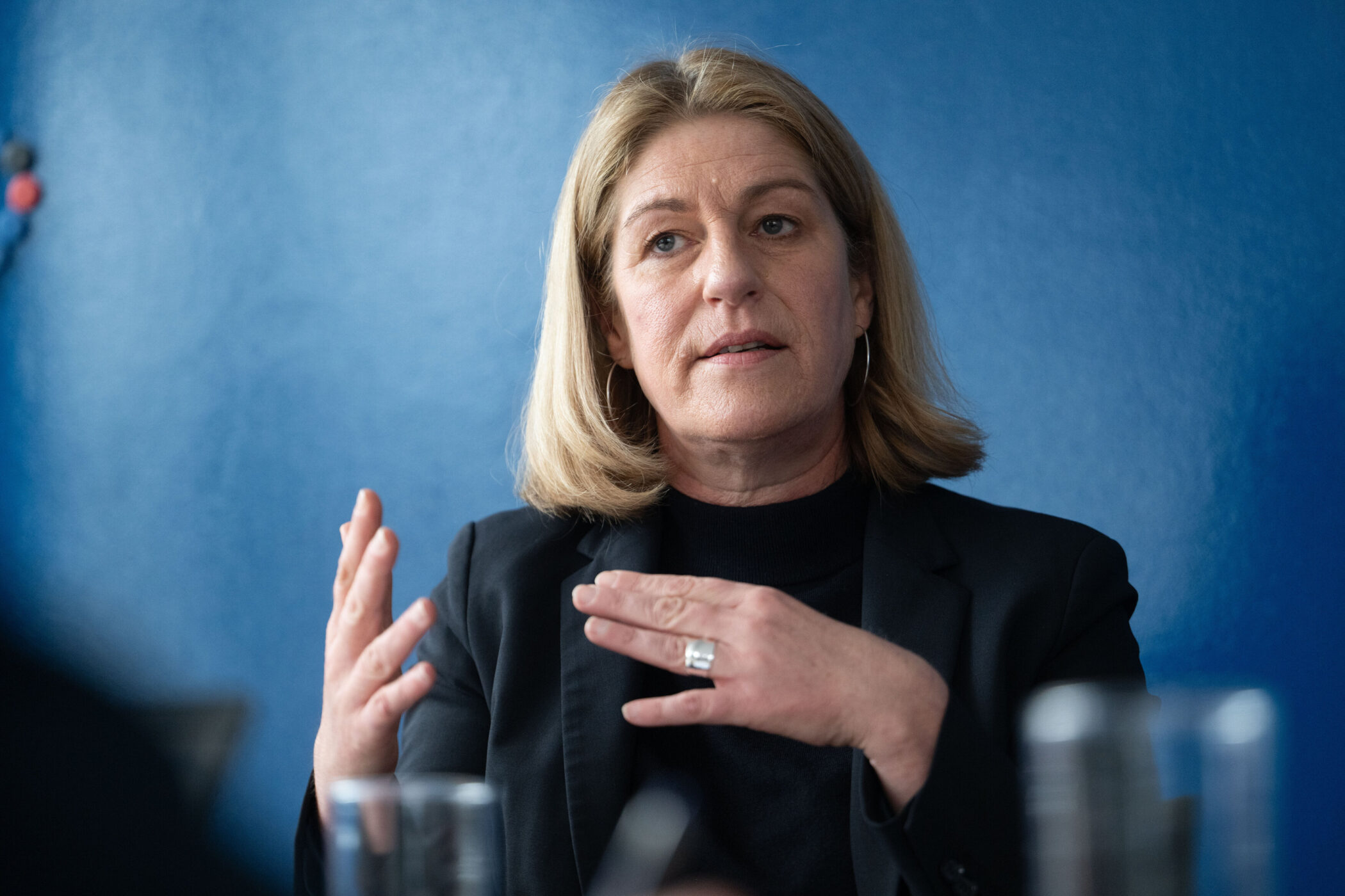 Eine Person mit blonden Haaren gestikuliert vor einer blauen Wand.