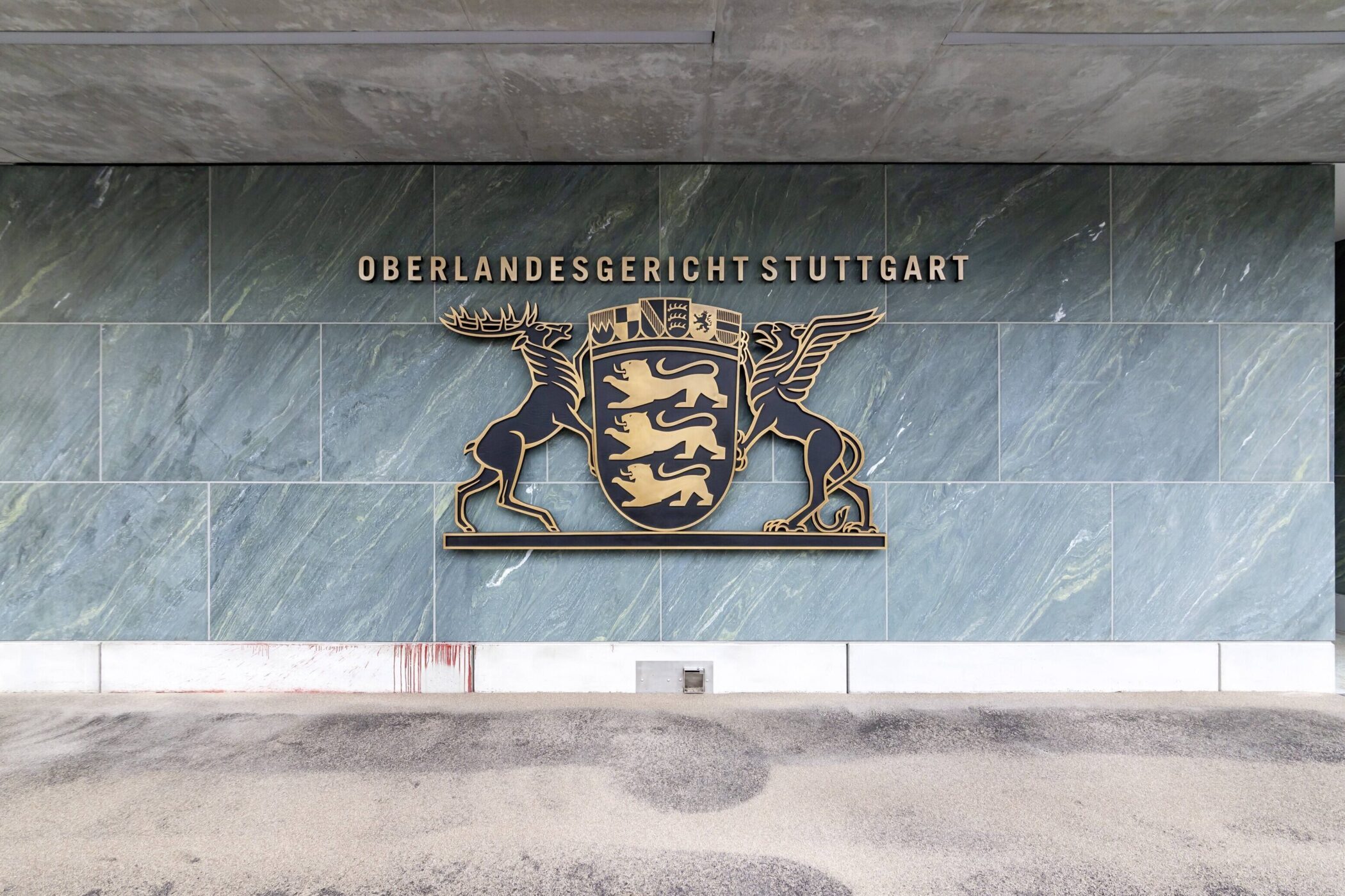 Wand mit Schild und Text „Oberlandesgericht Stuttgart“, darunter Wappen mit Hirsch.