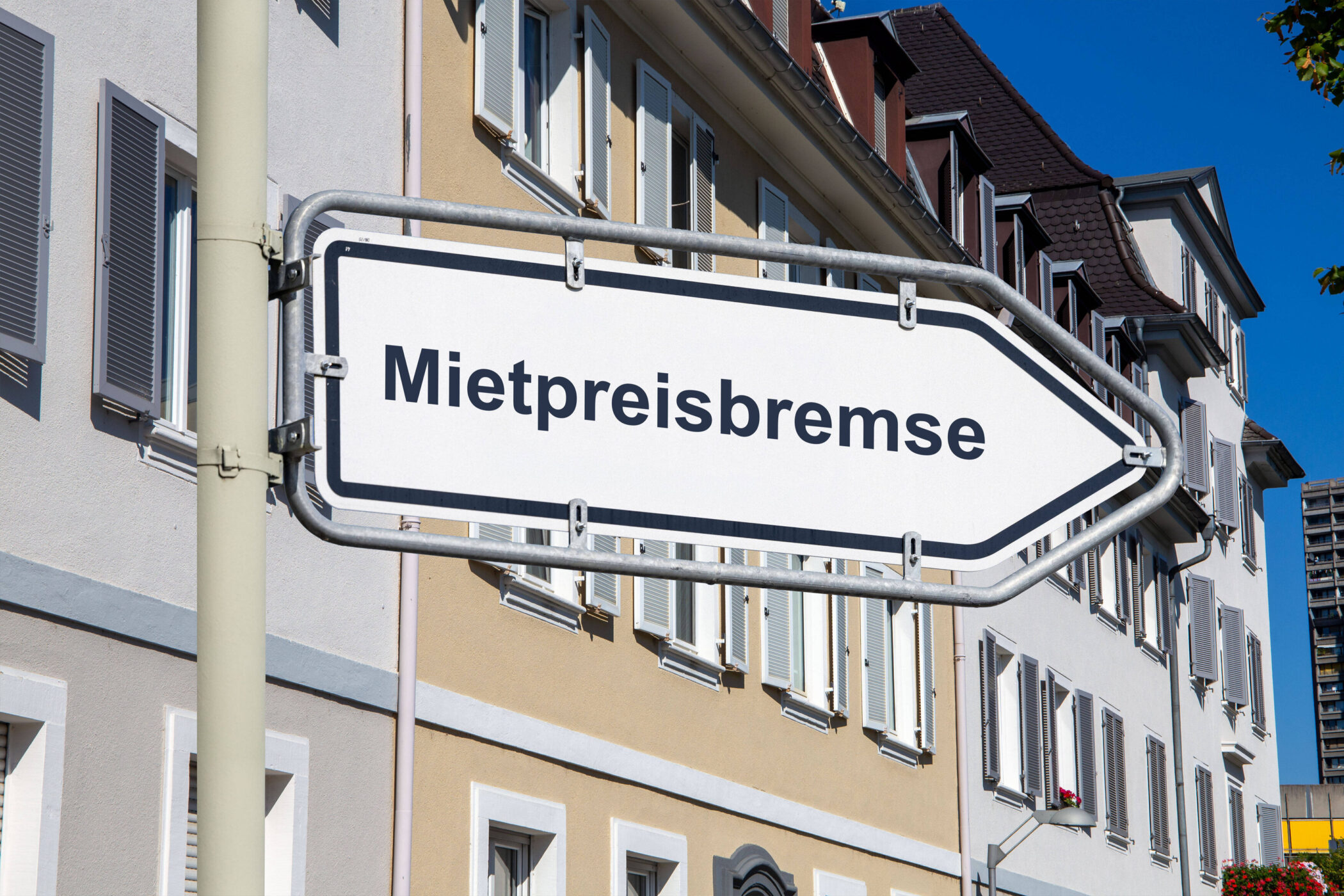 Straßenschild mit der Aufschrift "Mietpreisbremse" vor Gebäuden.