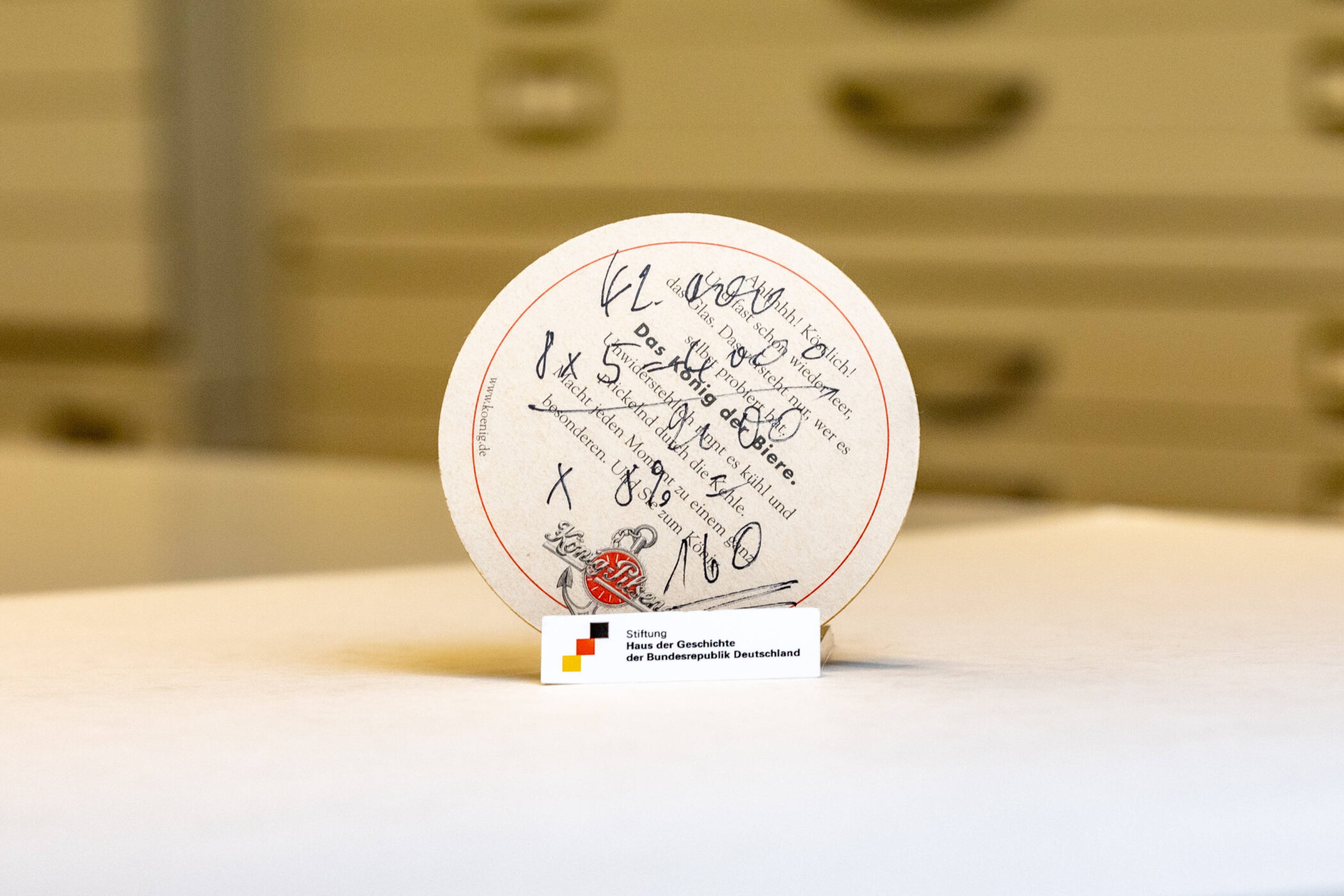 Runder Bierdeckel mit handgeschriebenen Notizen, Text teilweise lesbar.