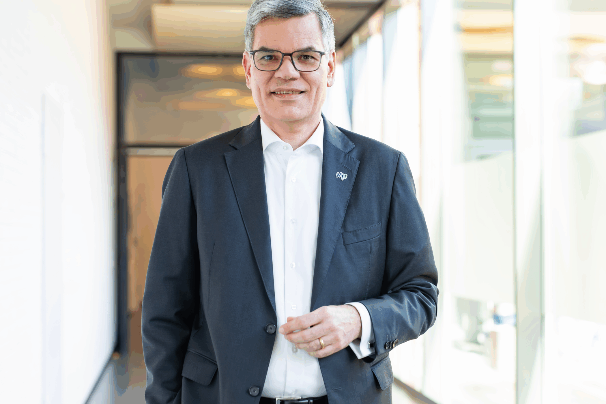 Mann in Anzug mit Brille steht in einem hellen Flur.