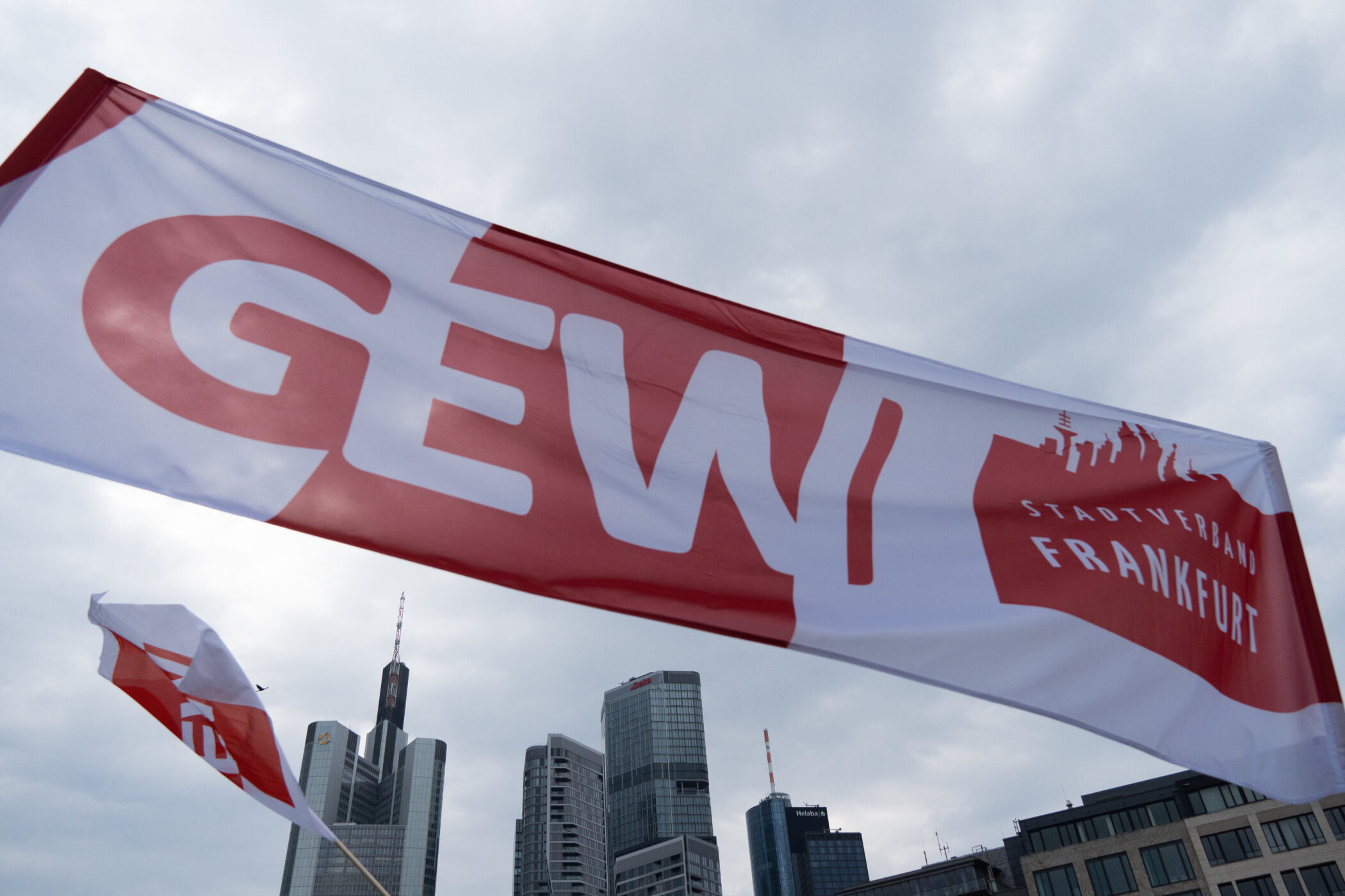 Große Fahne mit der Aufschrift "GEW, Stadtverband Frankfurt" vor Wolkenkratzer.