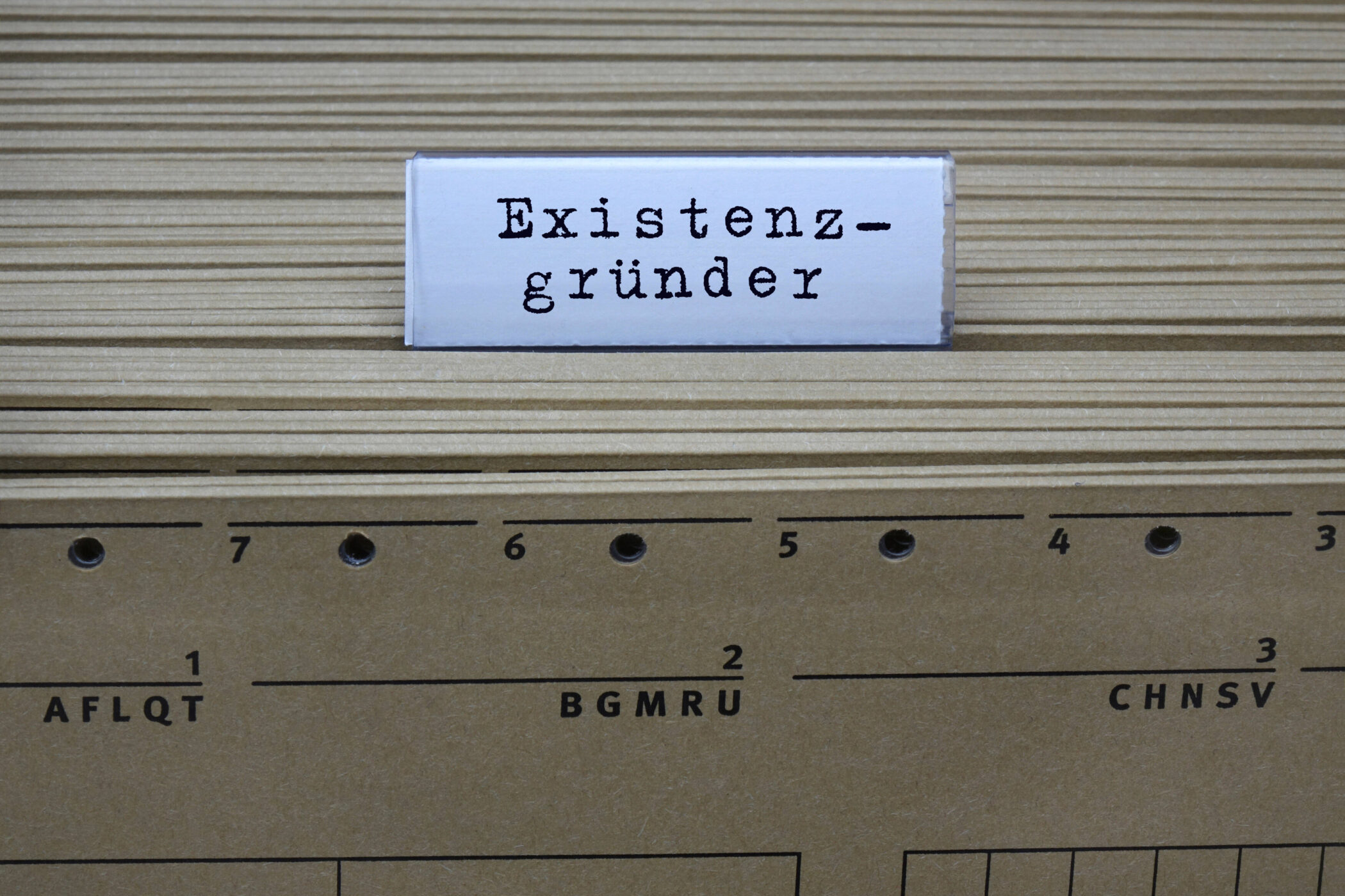 Schild mit Text "Existenzgründer" vor Aktenregistern mit Zahlen.