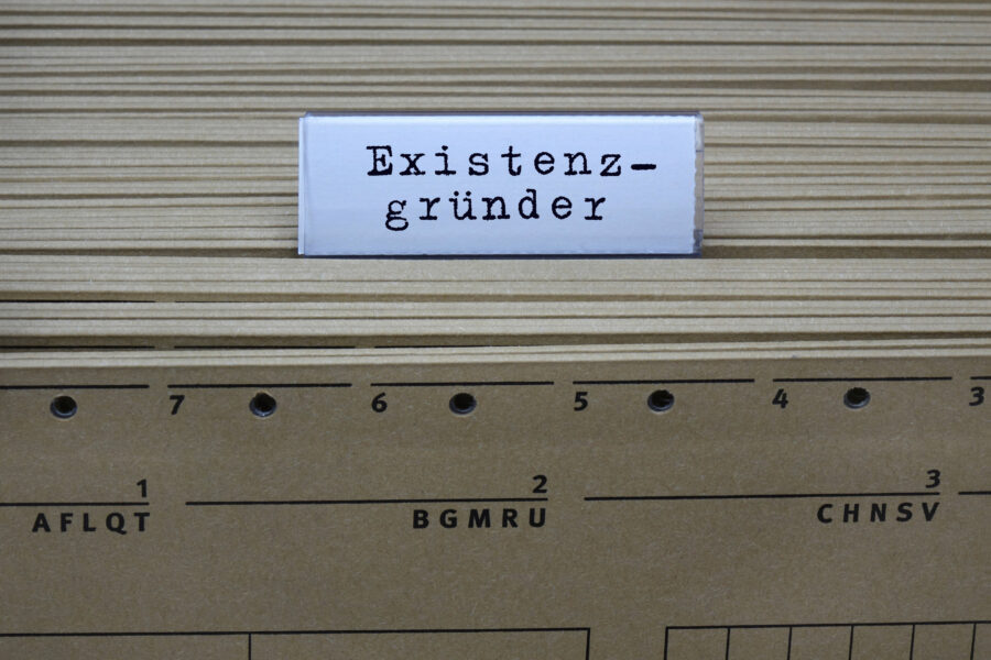 Schild mit Text "Existenzgründer" vor Aktenregistern mit Zahlen.