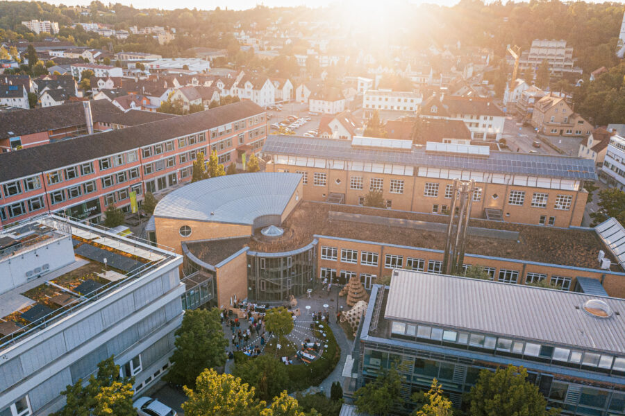 Luftaufnahme von Gebäuden mit Menschen im Hof und umliegender Stadtlandschaft bei Sonnenuntergang.