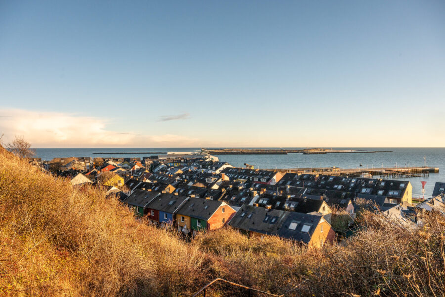 Blick auf bunte Häuser, Hafen und Meer bei klarem Himmel.