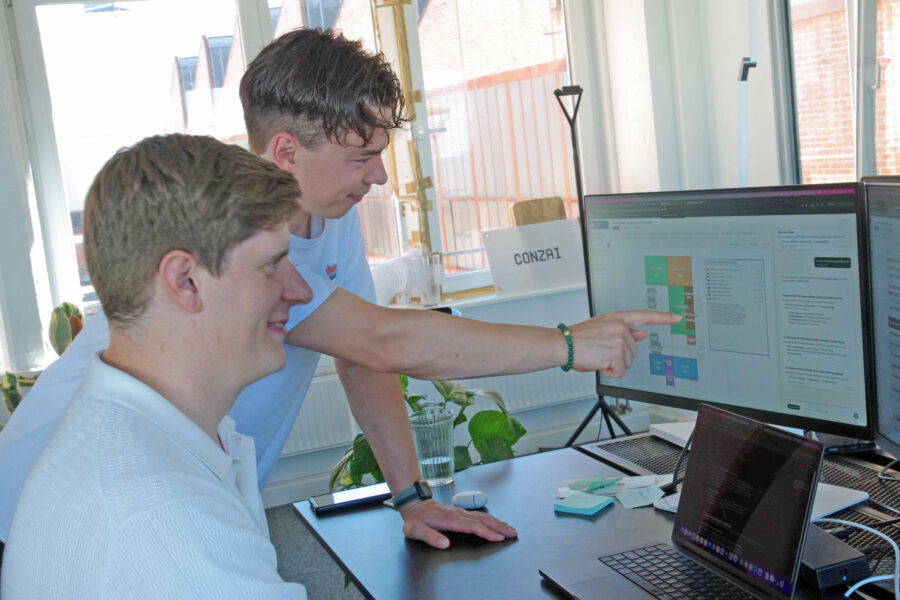 Zwei Personen arbeiten am Computer, eine zeigt auf den Bildschirm.