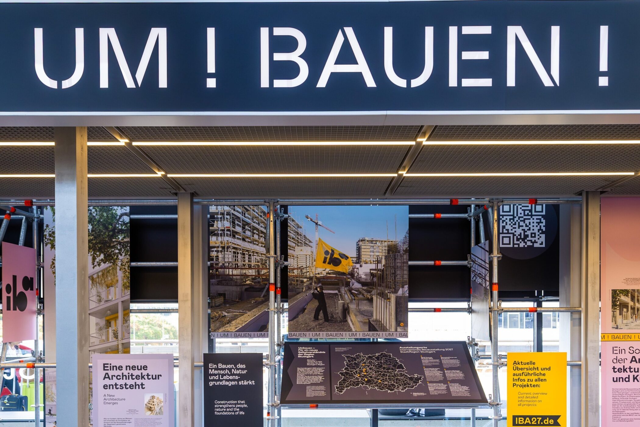 Schriftzug "UM!BAUEN!", Informationstafeln und QR-Code in einer Ausstellung.