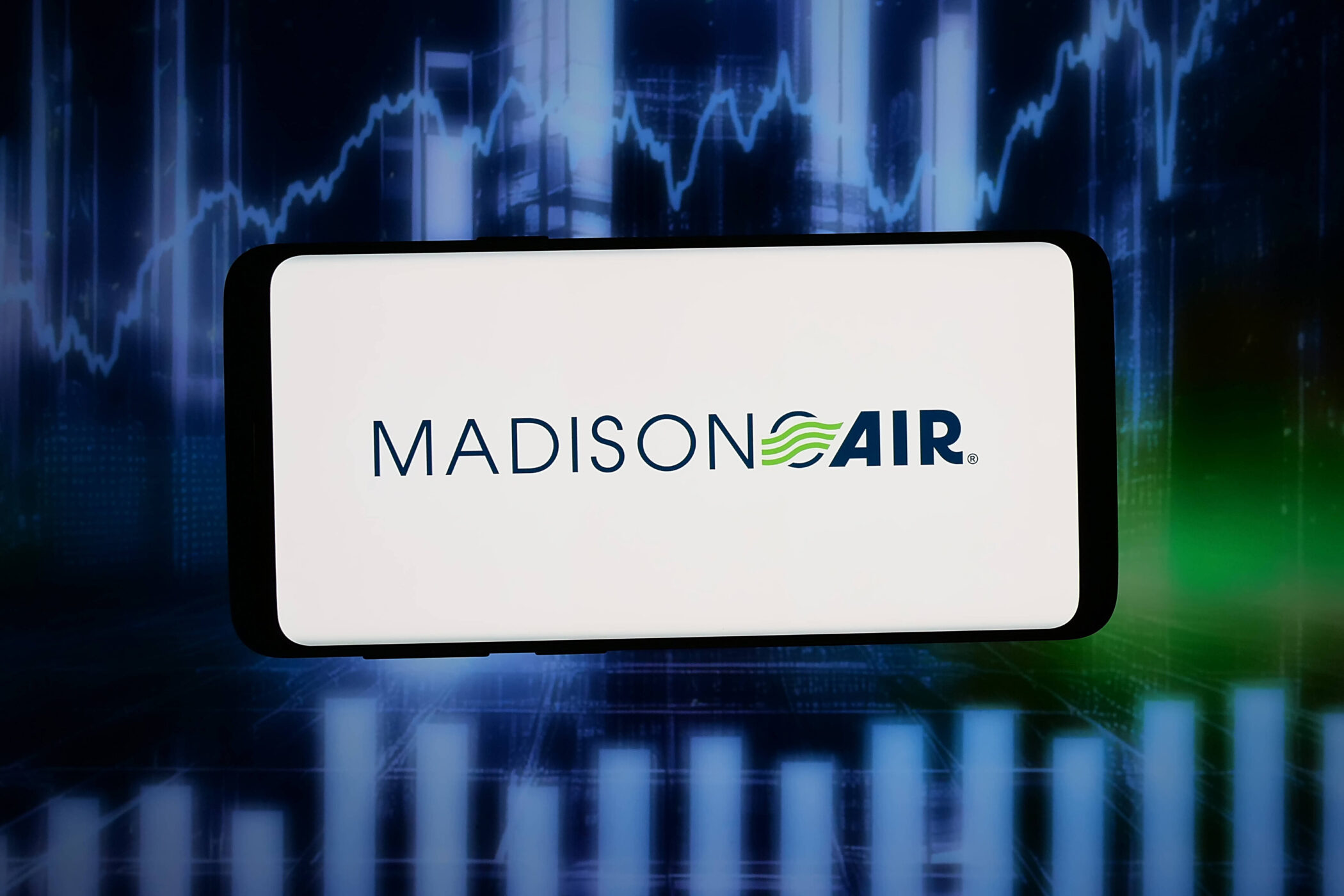 Smartphone zeigt „MADISON AIR“ vor blauem Bildschirm mit Diagramm.