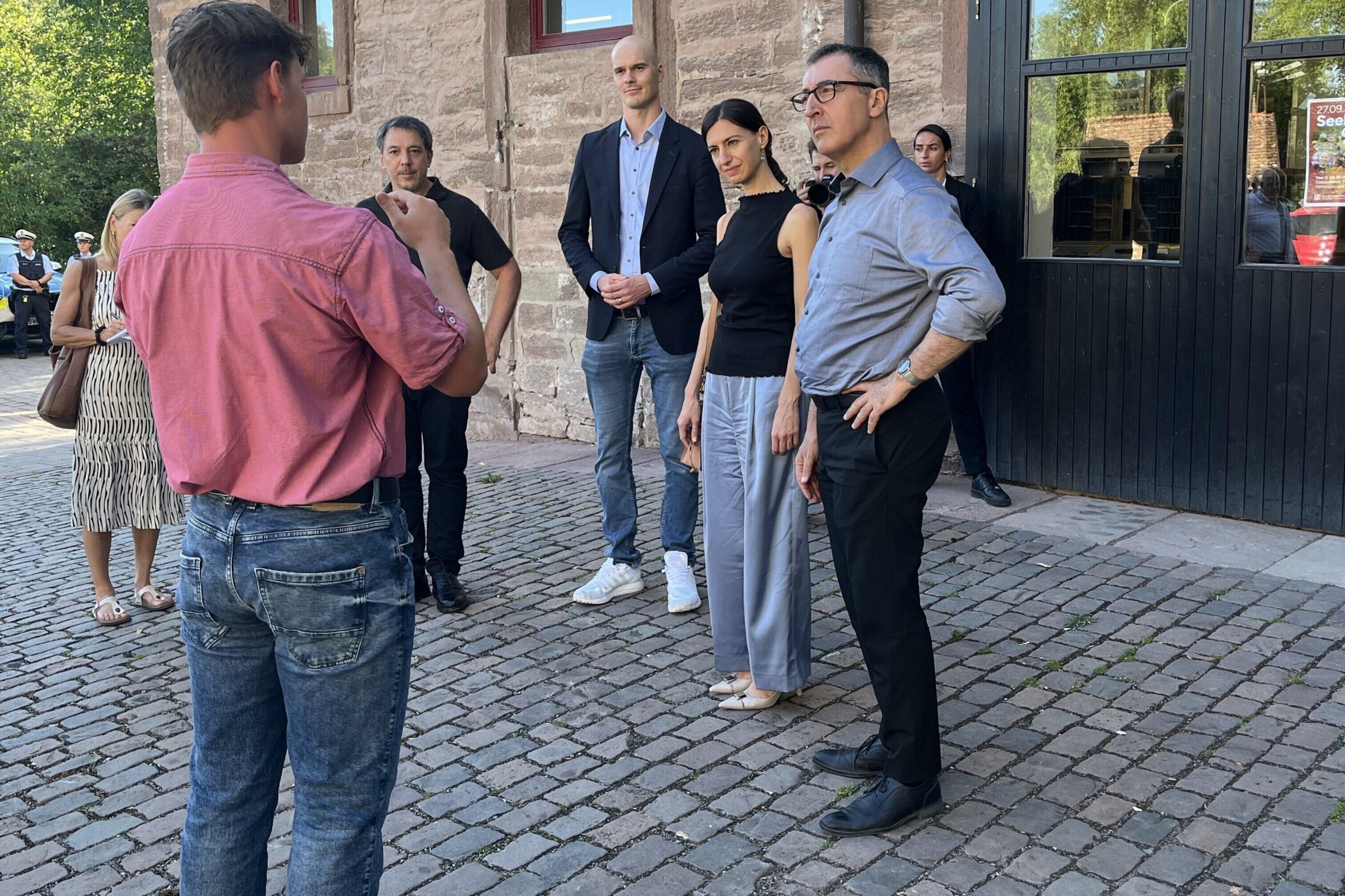 Fünf Personen stehen in einem Gespräch im Freien vor einem Gebäude.
