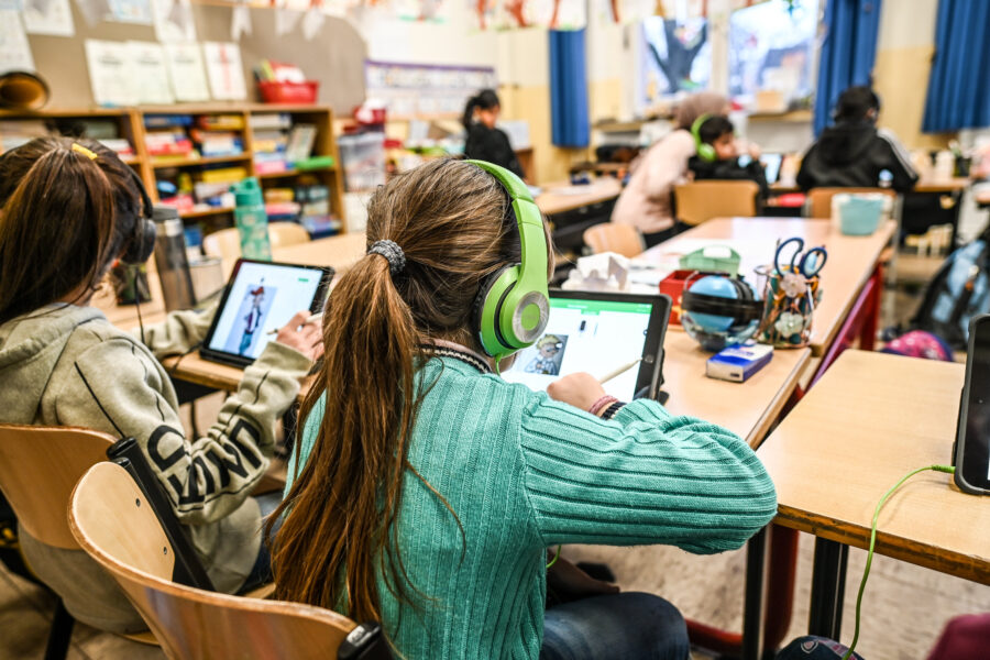 Mehrere Kinder an Tischen arbeiten mit Tablets in einem Klassenzimmer.