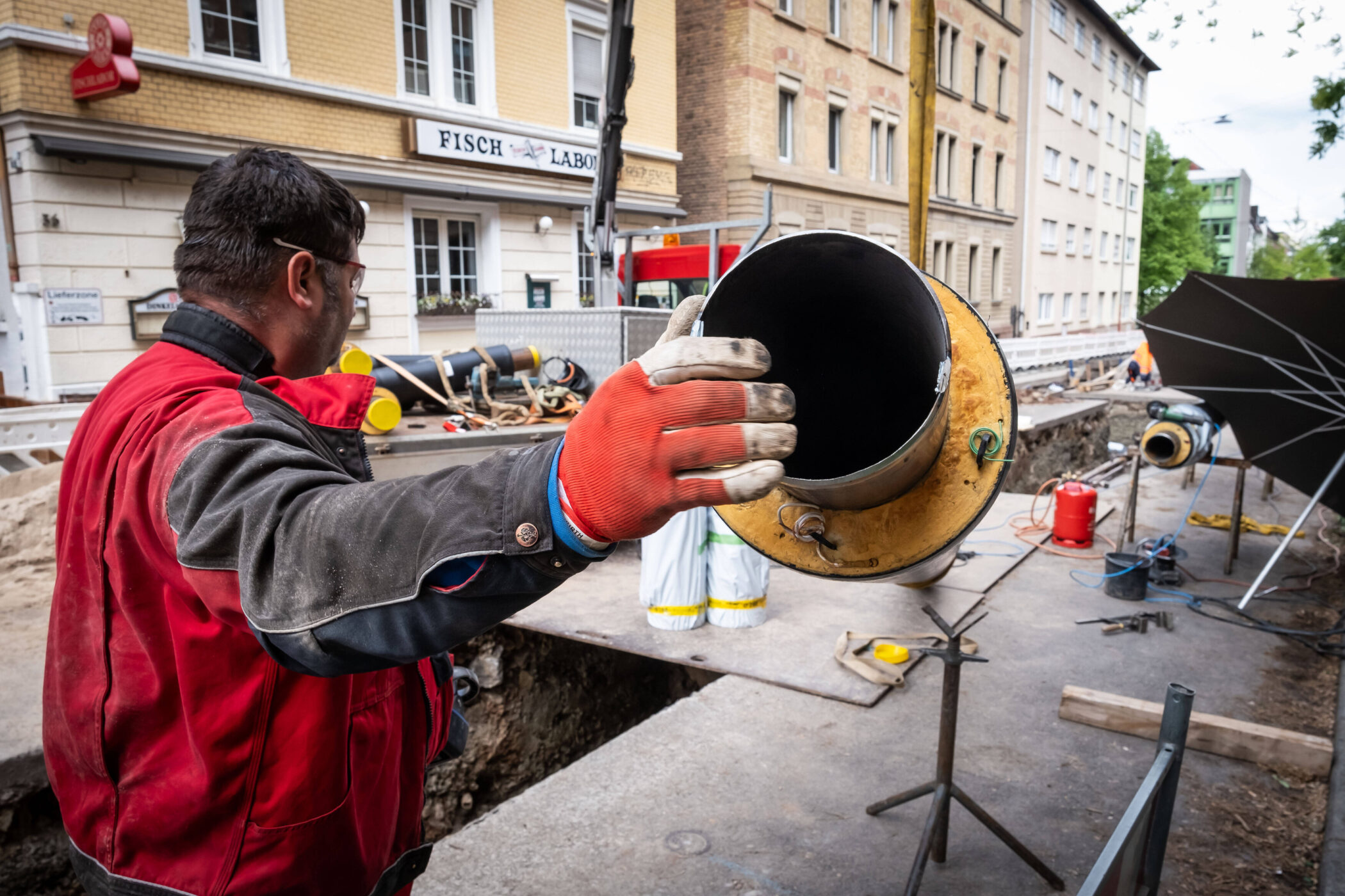 Ein Arbeiter hält ein großes Rohr, im Hintergrund eine Baustelle.