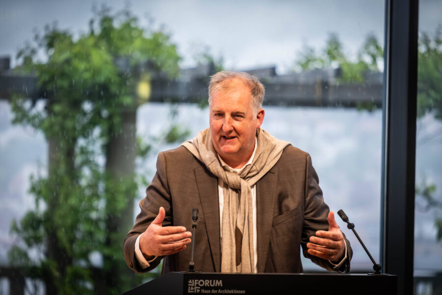 Mann in Anzug spricht an einem Rednerpult mit "FORUM" Aufschrift. Grüner Hintergrund.