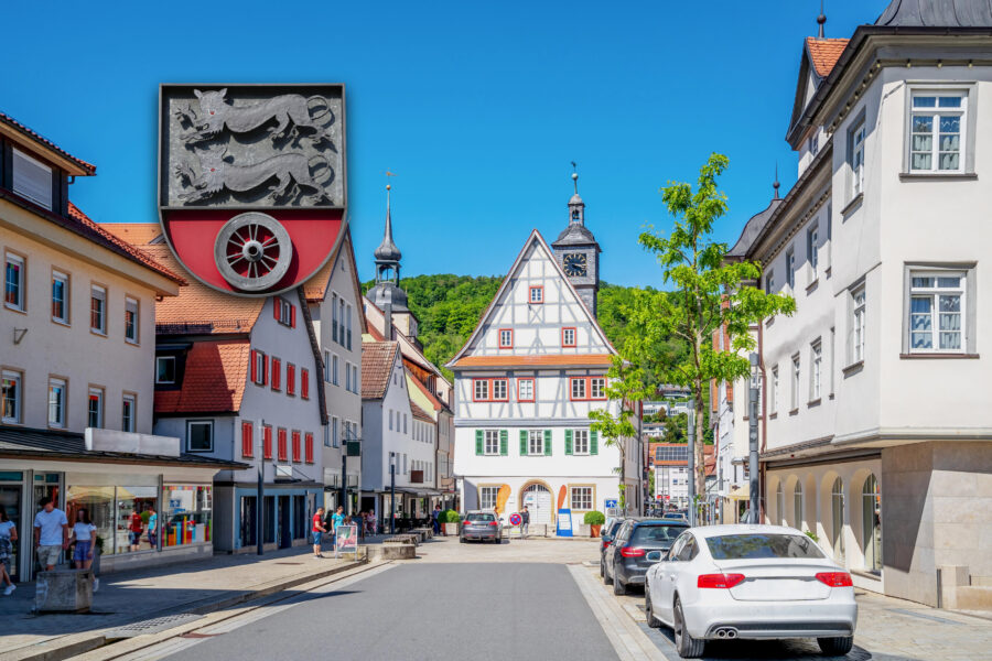 Straße mit Fachwerkhaus, Autos und Fußgängern, blauem Himmel, Wappen oben links.