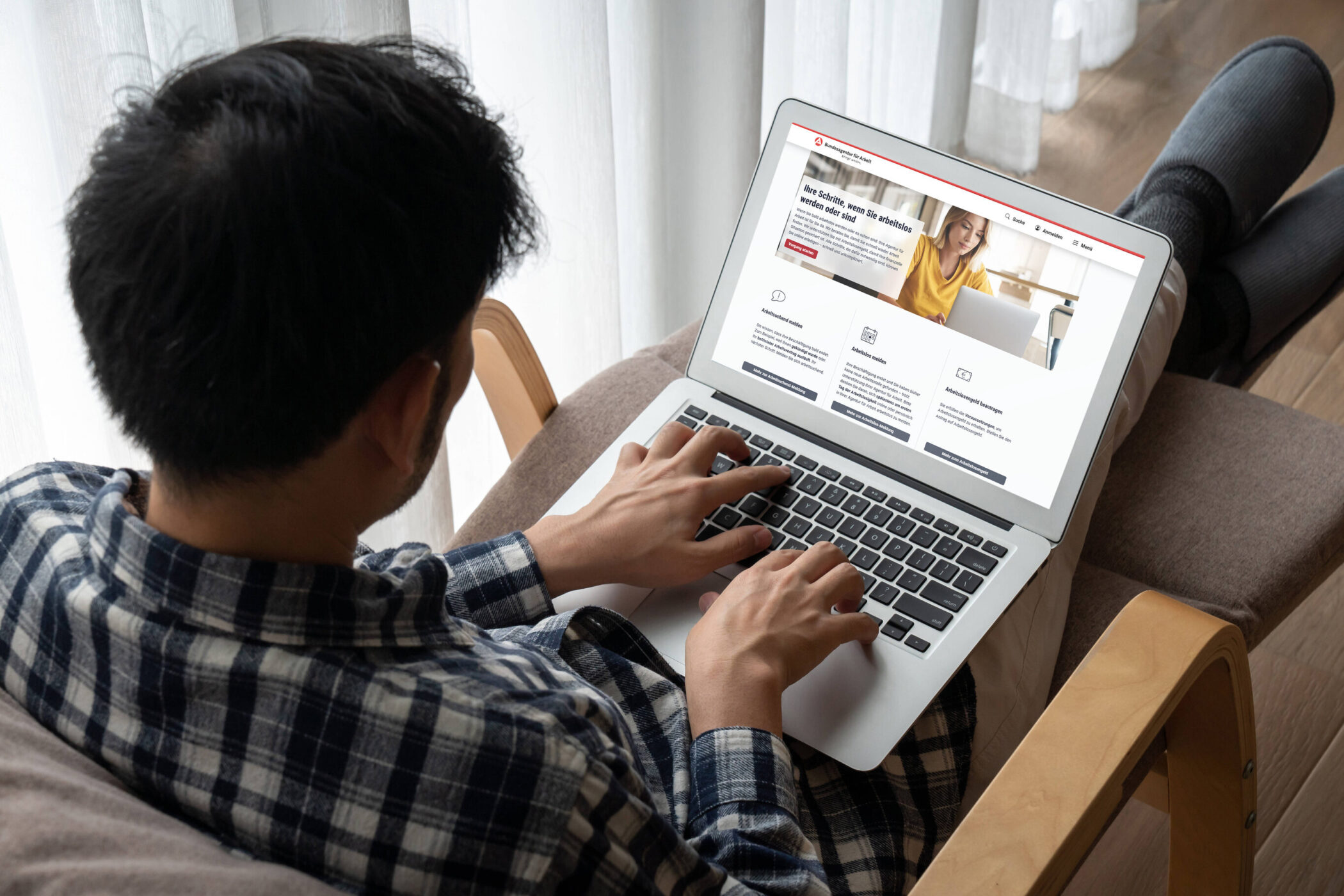 Person sitzt im Sessel und tippt auf Laptop mit Webseite.