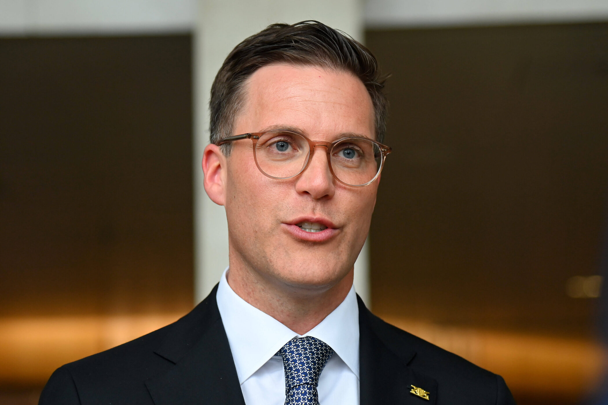 Mann mit Brille und Anzug, spricht, unscharfer Hintergrund.