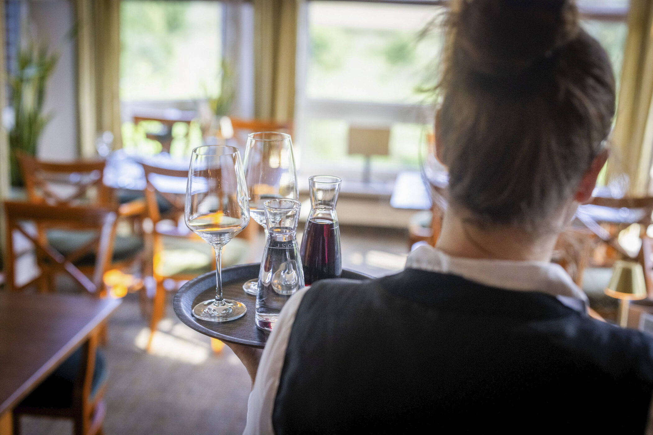 Person trägt Tablett mit Weingläsern und Karaffen in einem Restaurant.