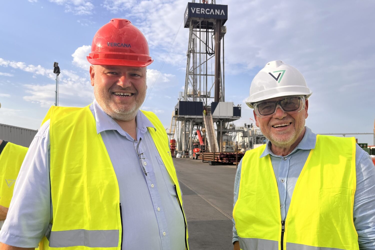 Zwei Männer mit Helmen und Warnwesten auf Baustelle, im Hintergrund Metallgerüst.